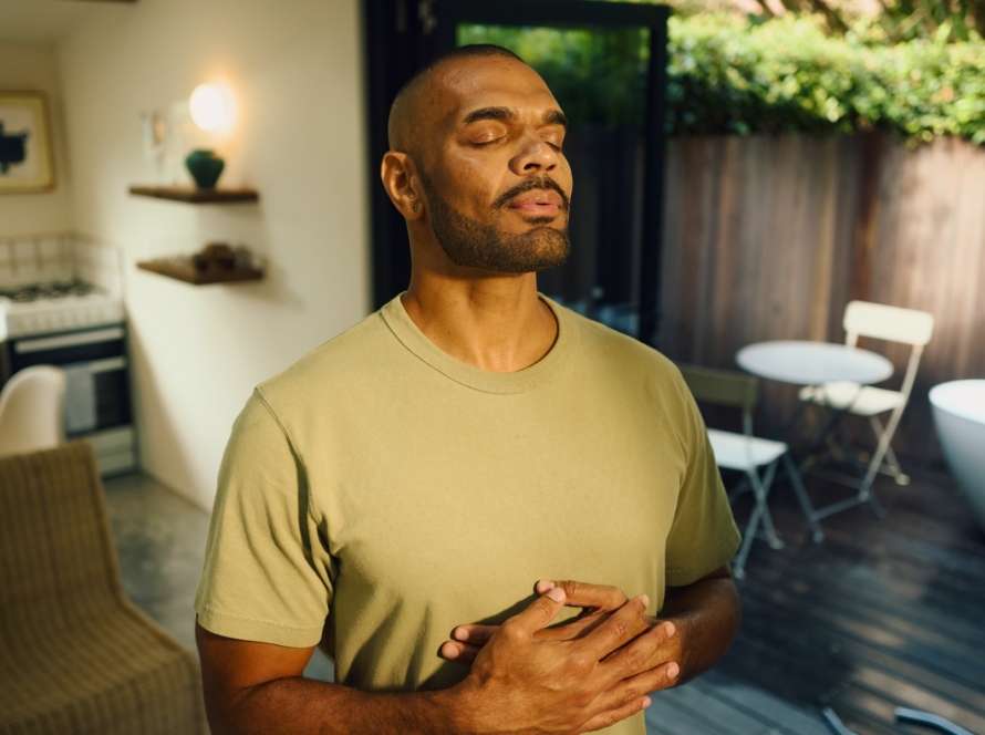 Serene young aboriginal australian man practicing mindfulness, taking deep breaths with closed eyes and hands on chest, enjoying a peaceful morning at home